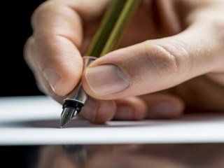 Close up of the hand of a man writing a letter or notes with a fountain pen on a sheet of paper or signing a document or contract